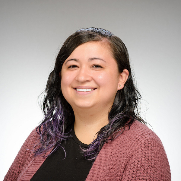 Michelle Luna. Smiling woman with dark, wavy hair and subtle purple streaks, wearing a black top and a textured dark pink cardigan.